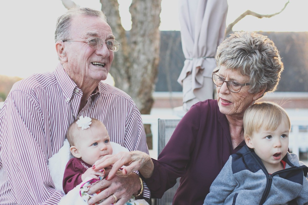Grandparents outdoors with two young grandchildren, all smiling.