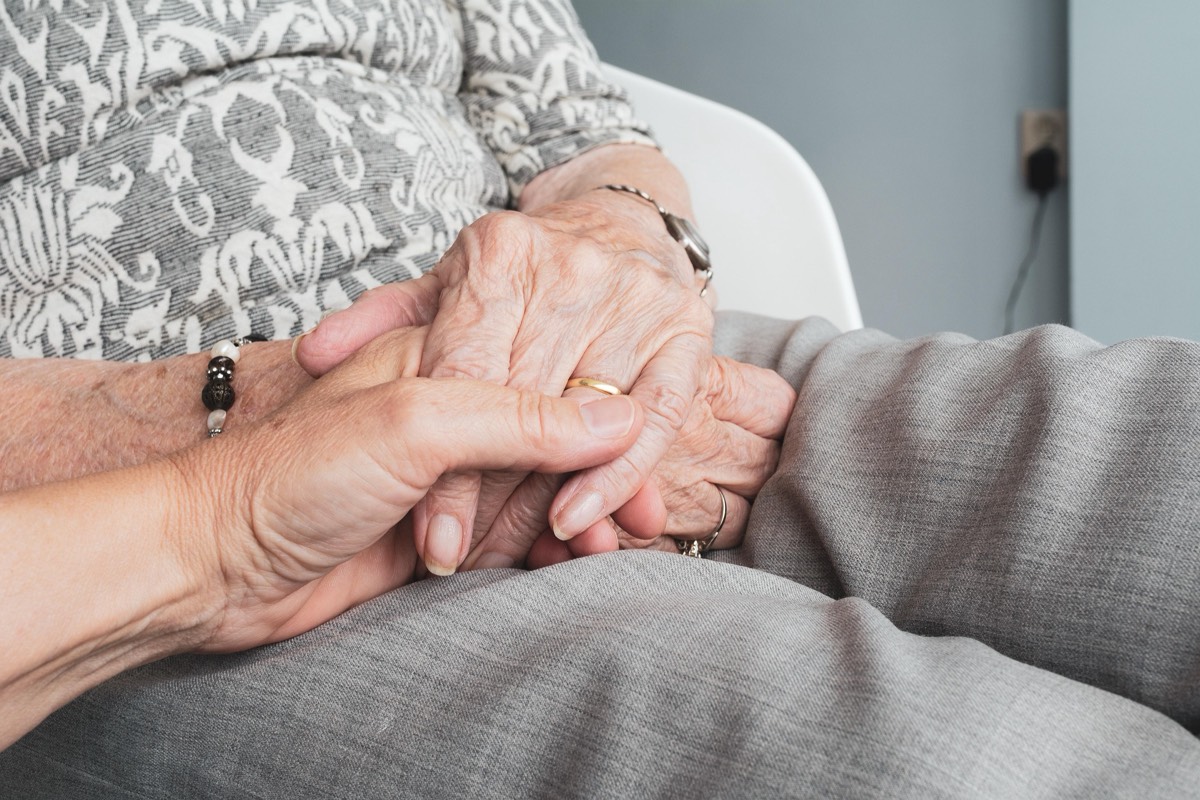A pair of younger hands gently holding an older person's hands.
