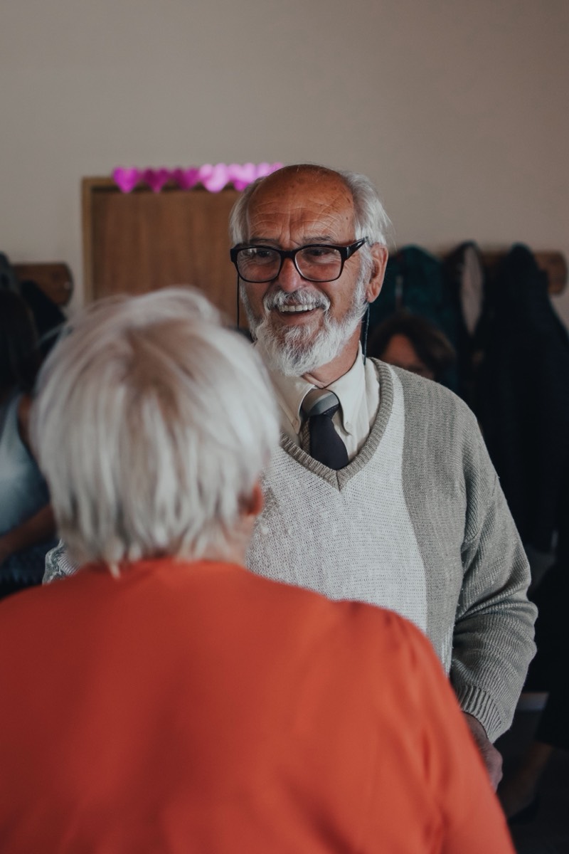 An older man smiling warmly as he greets someone with a hug.